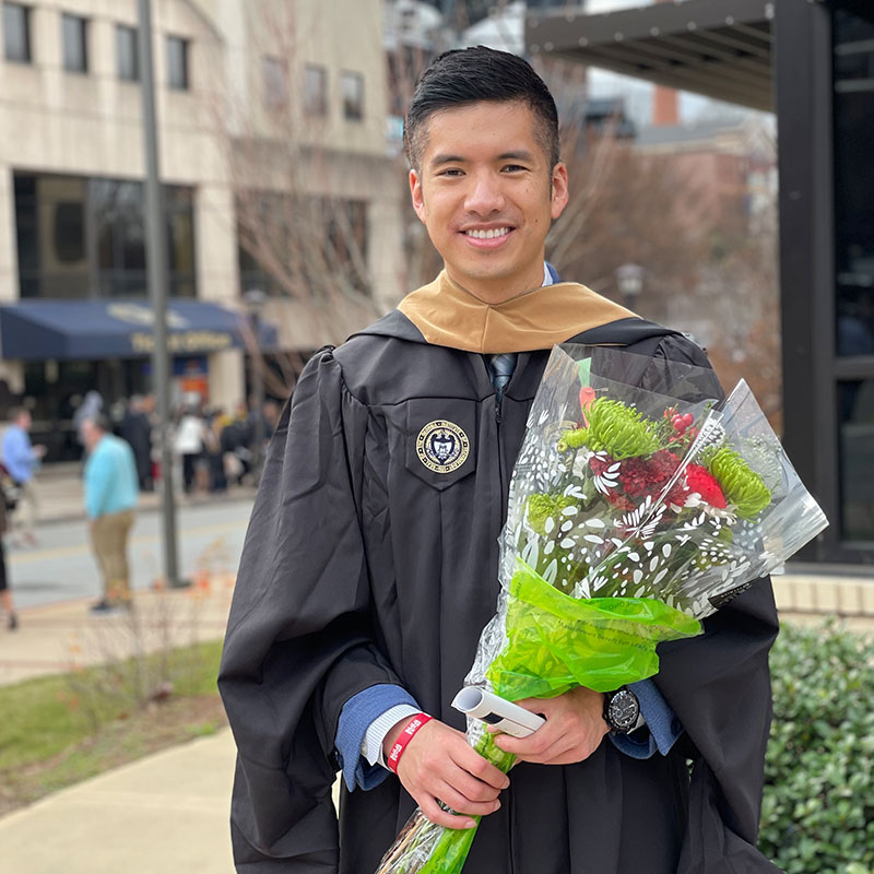 Phong Truong standing outside after graduation and holding a bouquet.