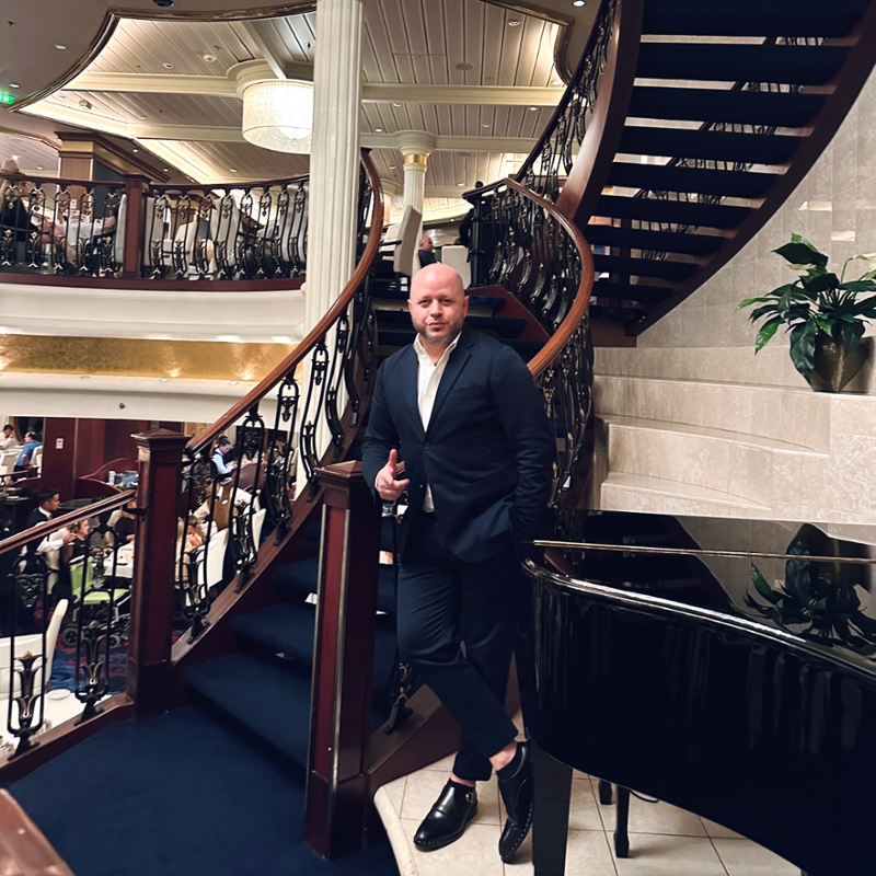 Sergio Guifarro, Scheller Evening MBA ‘24, stands leaning on a spiraled staircase next to a black grand piano.
