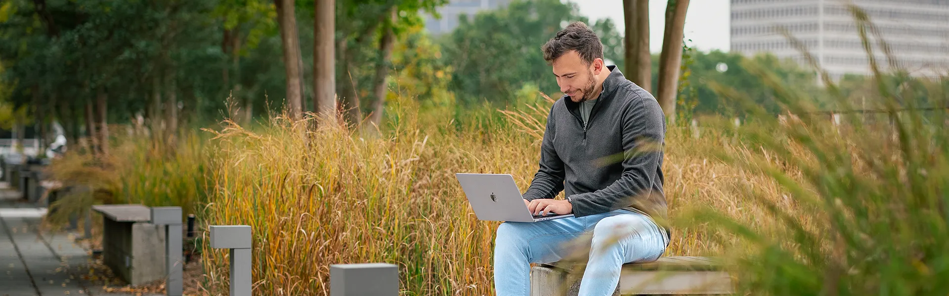 PhD Student outside on laptop sitting on bench