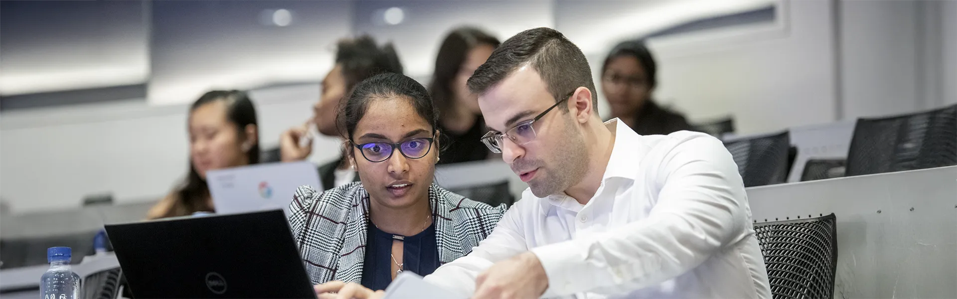 Two students in class reviewing information on laptop together