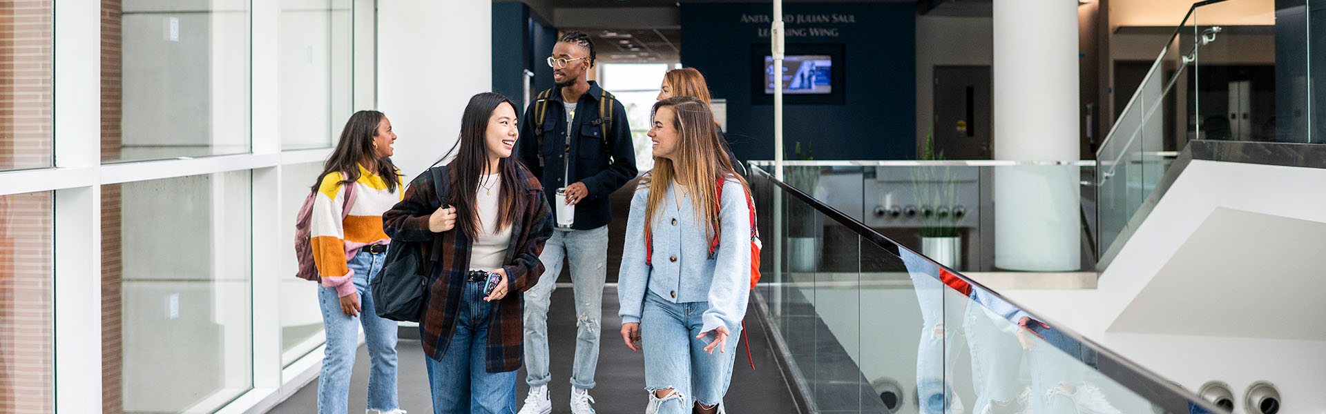 Five Scheller undergraduate students, with backpacks, walking across atrium bridge  