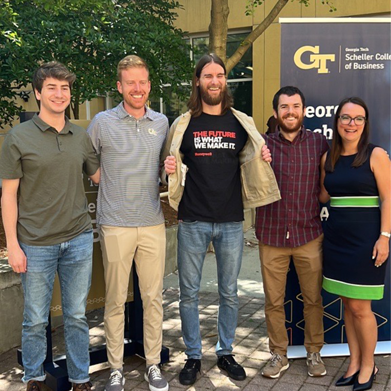 Scheller MBA students-four men and one woman-stand next to each other at the bell ringing ceremony