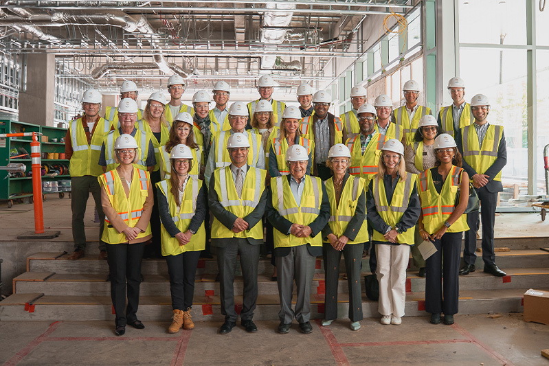 A group of people smile in hard hats and fluorescent vests