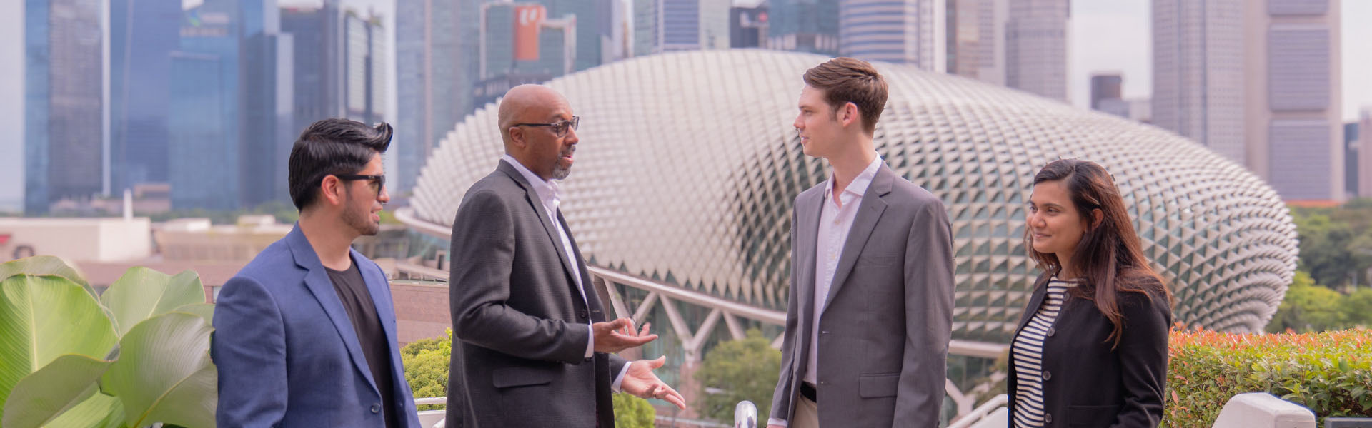 Group of four people talking outdoors in an urban setting with modern architecture in the background