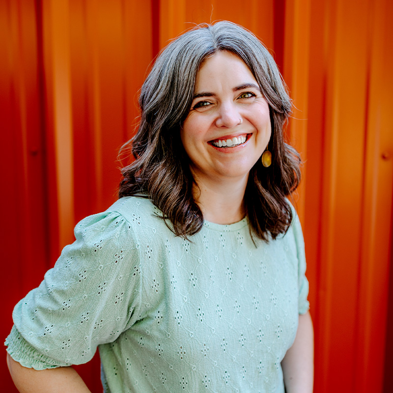 A woman smiles in front of an orange background