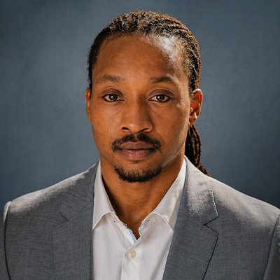 Jordan Page looks into the camera in a gray suit jacket.