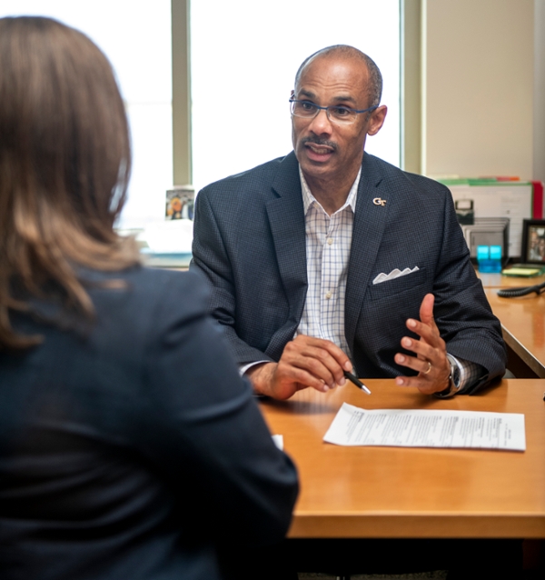 A man sits at a desk and is showing a woman a piece of paper.