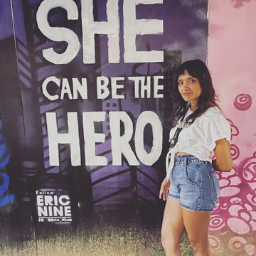 A student standing in front a billboard that reads she can be the hero