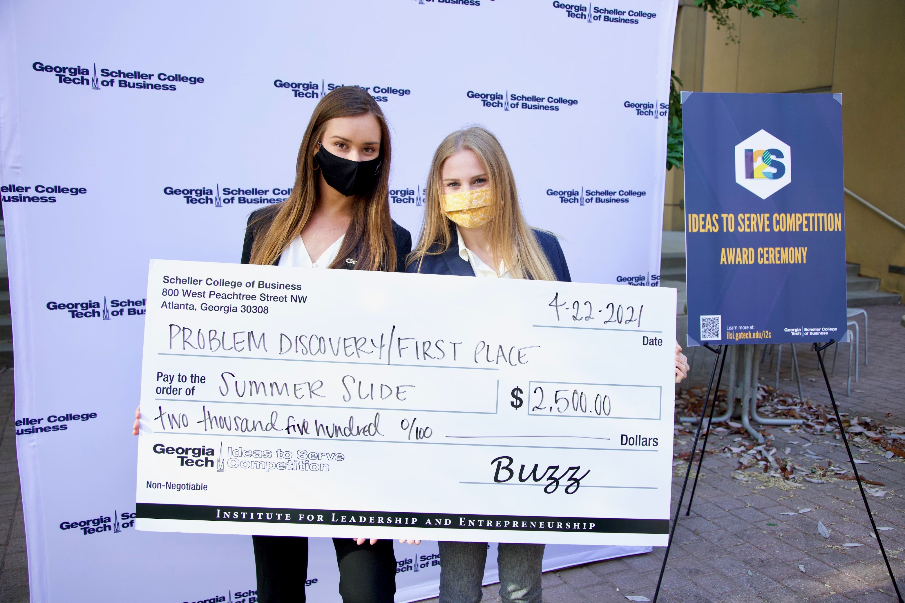 Two Georgia Tech students holding up a large check after winning the Problem Discovery track at the Ideas 2 Service competition. 