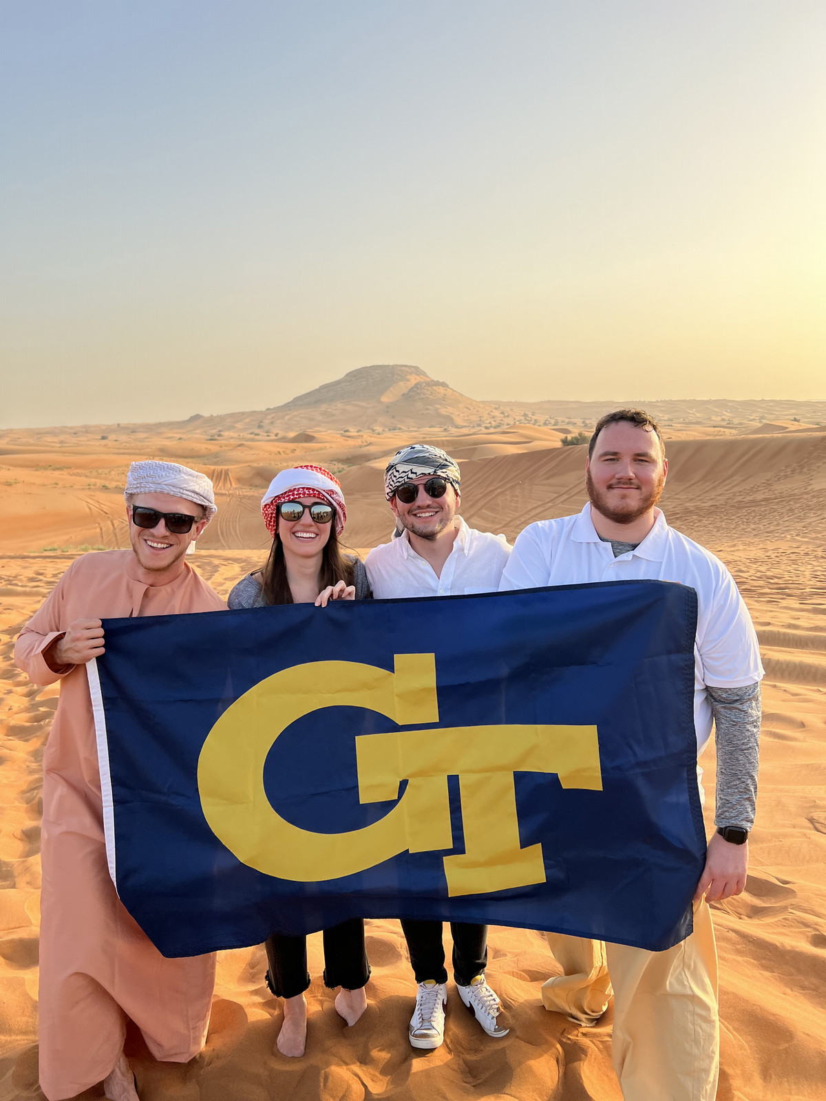 A group of students hold a Georgia Tech flag in the desert