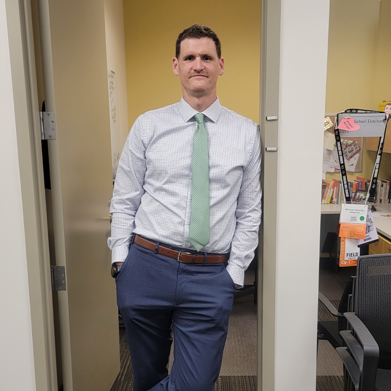 Michael Dutcher, director of undergraduate career education at Scheller, stands in the Scheller building atrium in a suit and tie. 