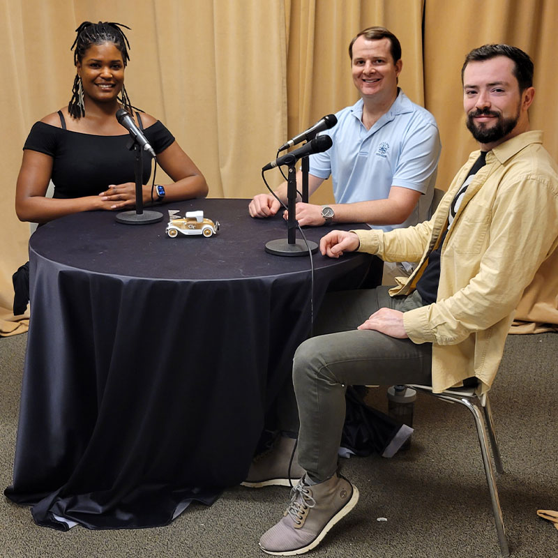 One woman and two men sitting together at a table with microphones. 