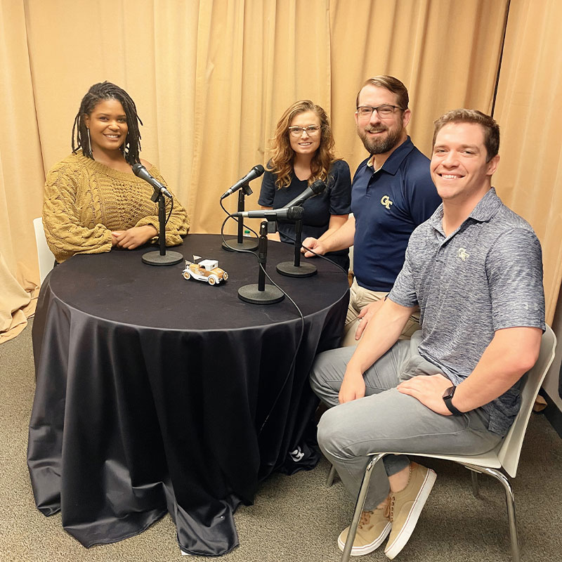 Four people sitting around a table to record a podcast episode.