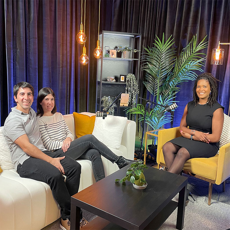 Two women and one man sit around a microphone.  