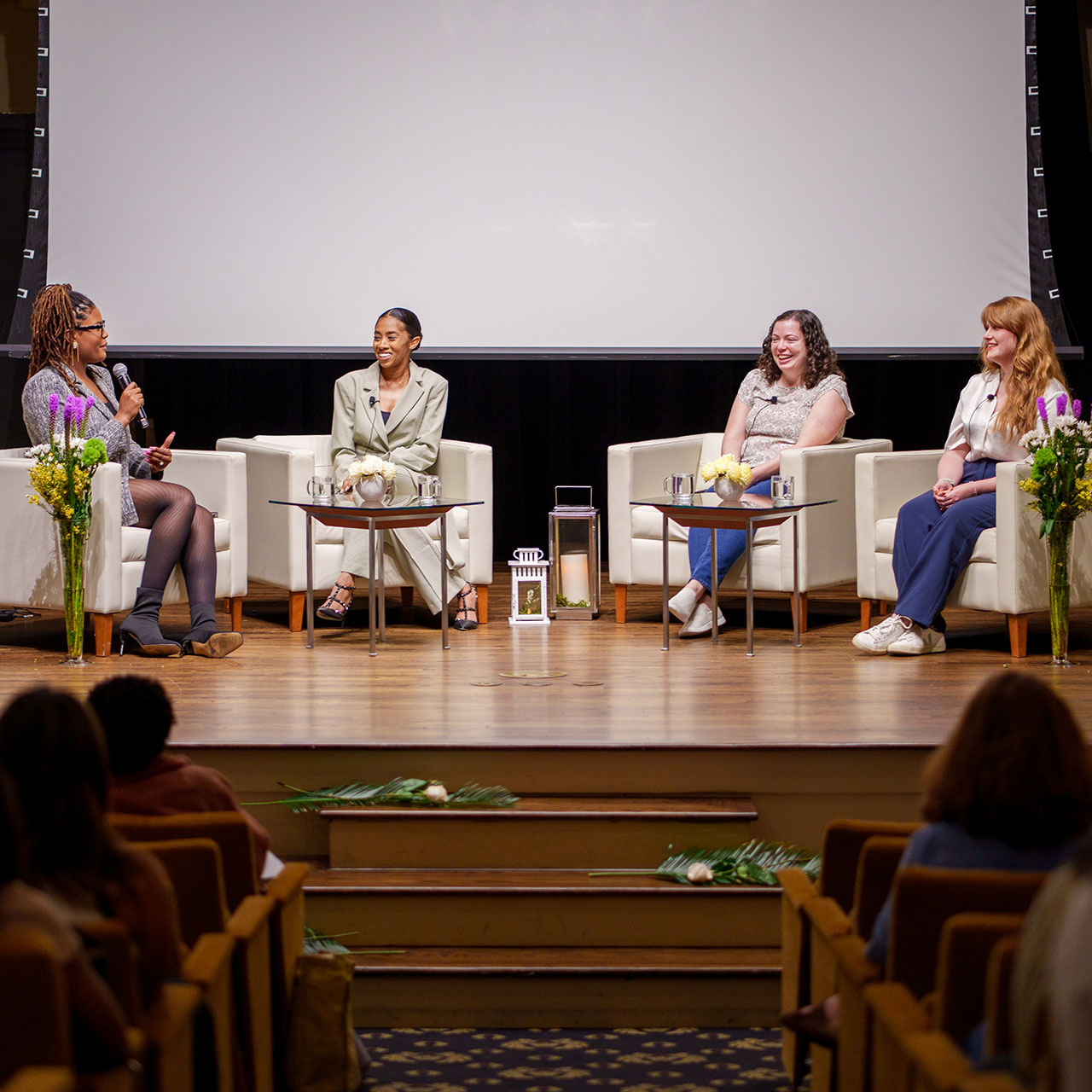 Four women sit on white chairs on a stage participating in a panel discussion.    