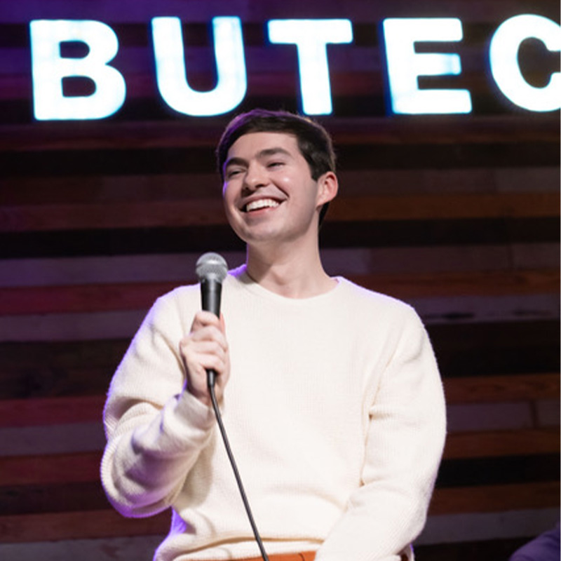 A man smiles on a stage holding a microphone.
