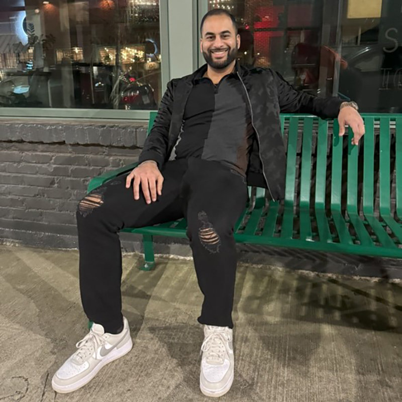 A man casually sits on a green bench 