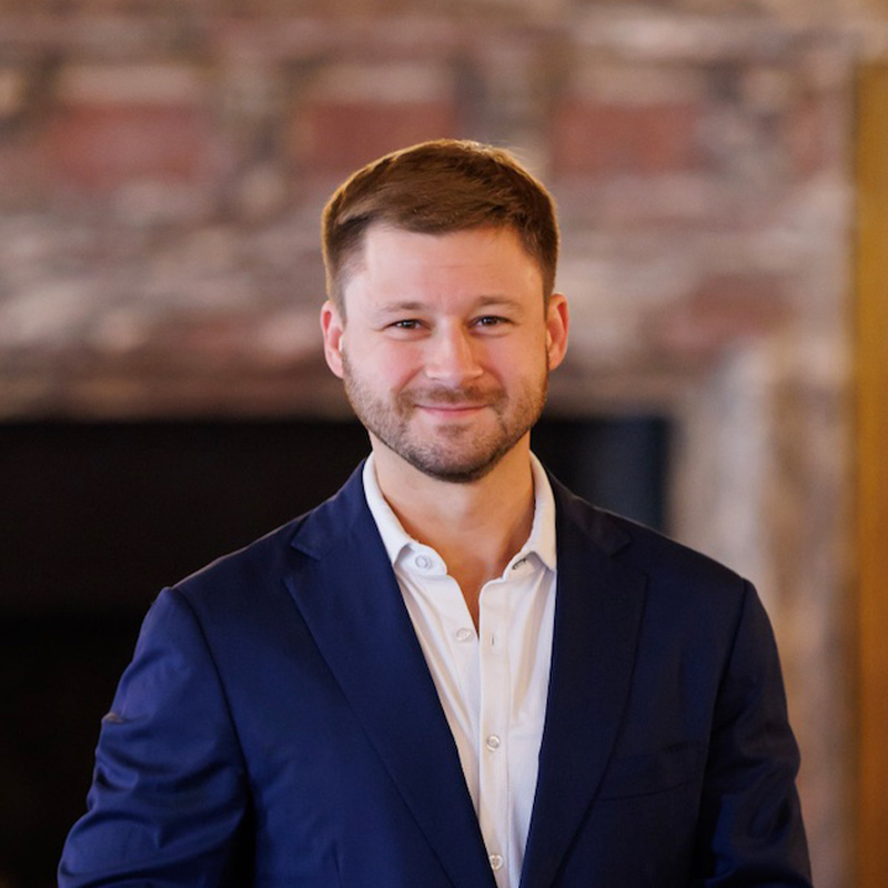 A man smiles in a suit jacket 