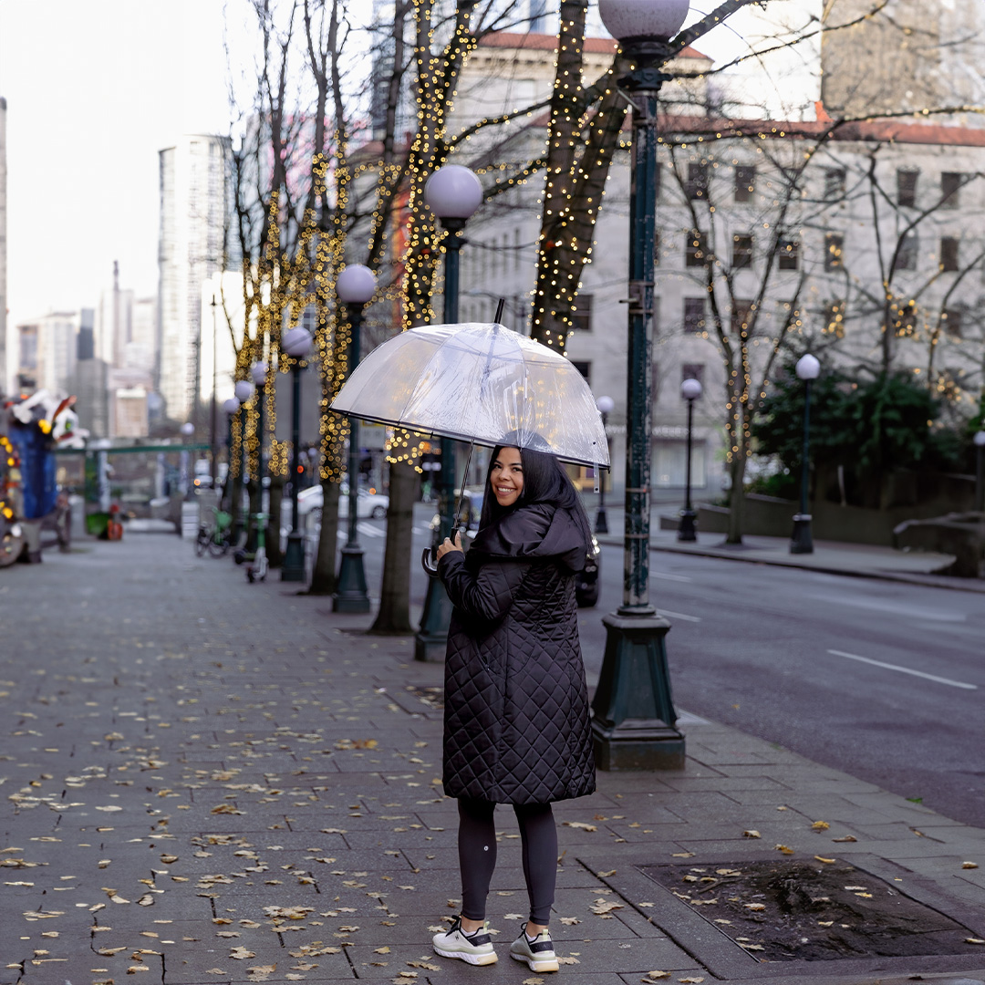  I woman stands on a city sidewalk holding an umbrella 