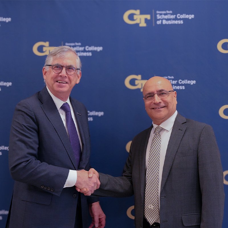 Two men in suits smile and shake hands