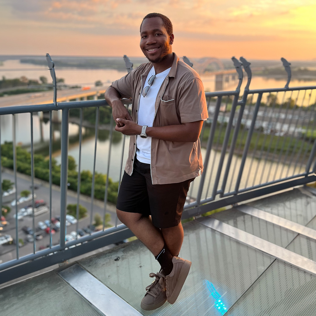 man standing on rooftop against a sunsetted harbor 