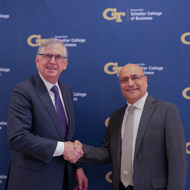 Two men in suits smile and shake hands