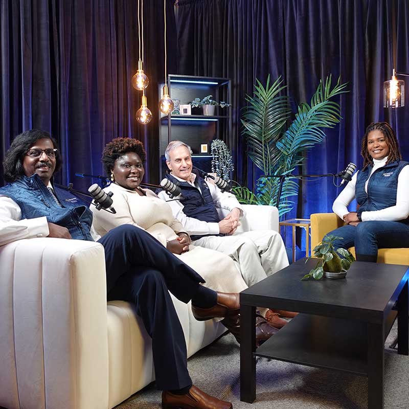 Two women and two men sitting on sofas speaking into microphones. 