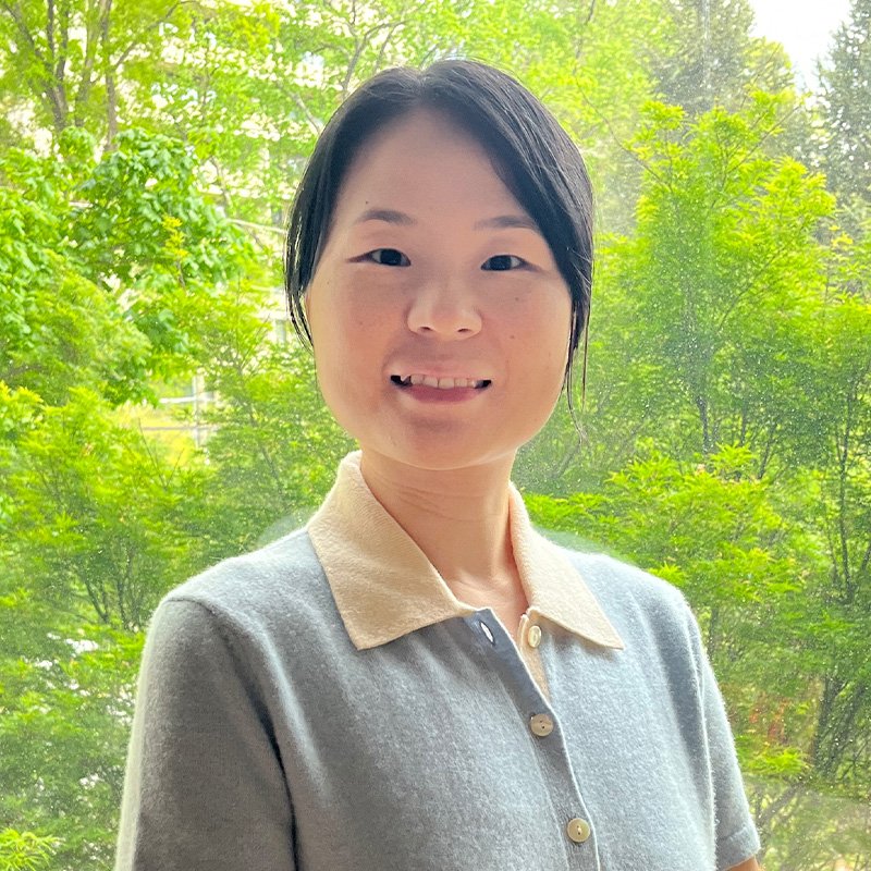Ting Chen smiles standing in front of leafy, green trees