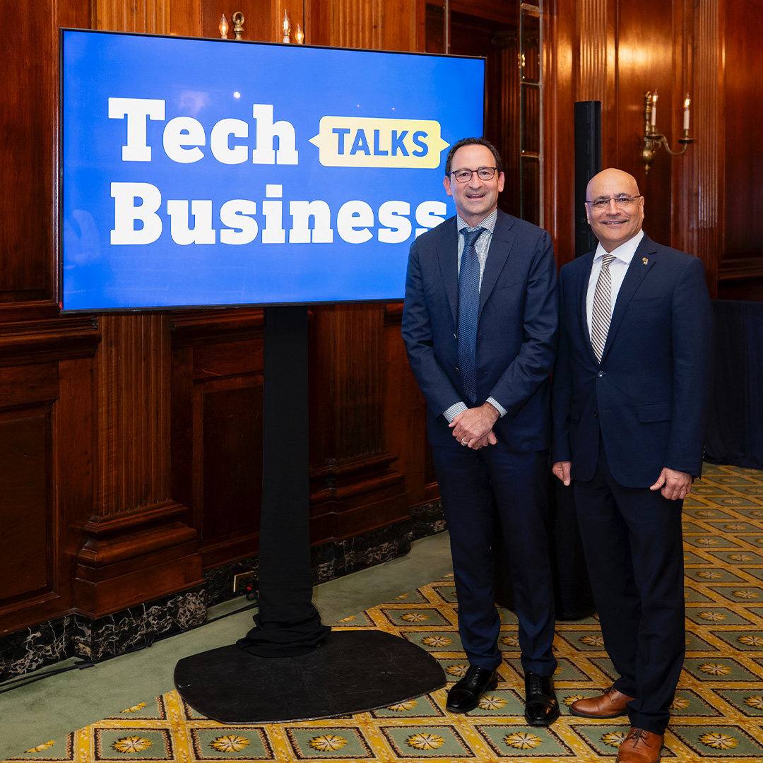Two men stand in front of a sign