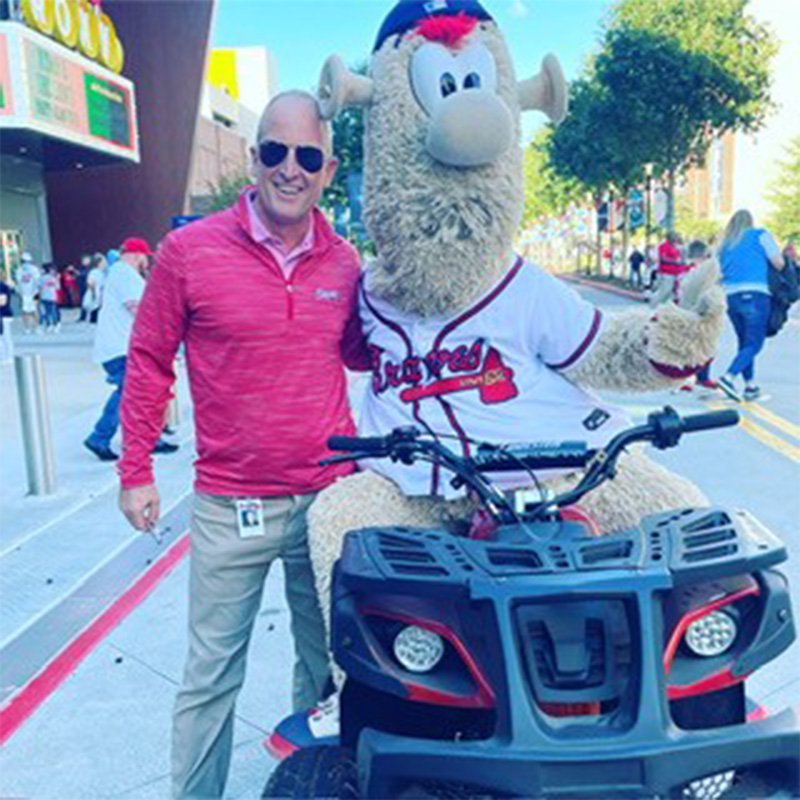 Adam Zimmerman, senior vice president of marketing and content for the Atlanta Braves, smiles next to Blooper, the Braves team mascot.