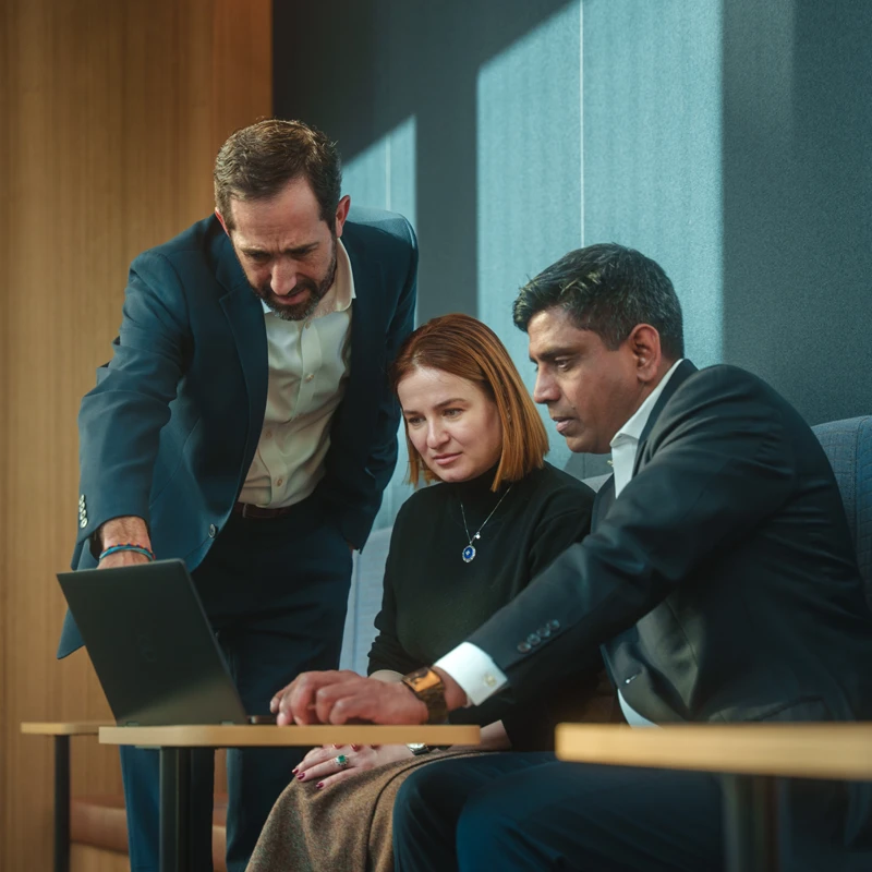 Three people are working on a laptop in a modern office setting.