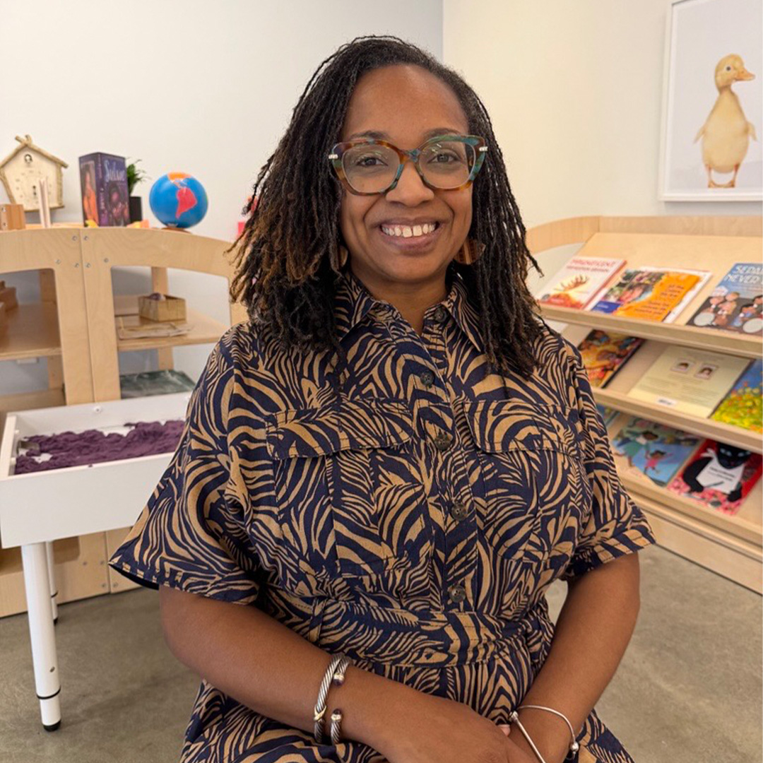 Brandi Biscoe Kenner, Ph.D. and Executive MBA ‘26, and current chief learning officer at Bezos Academy sits in a classroom with children’s books in the background.