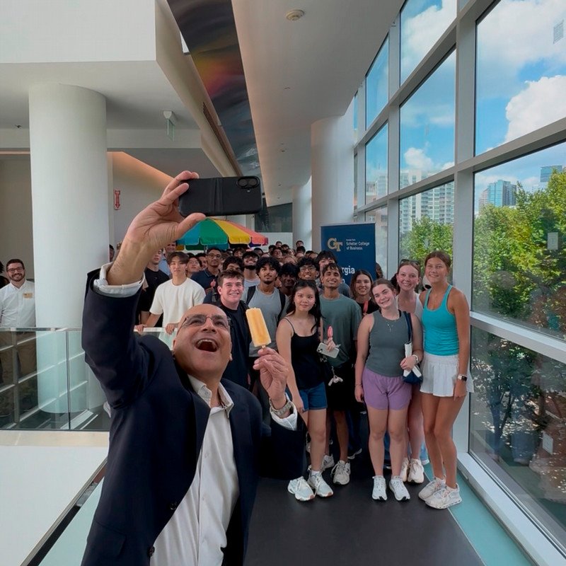 Dean Anuj Mehrotra holds a popsicle while posing with a large group of Scheller students during a Welcome Week event.