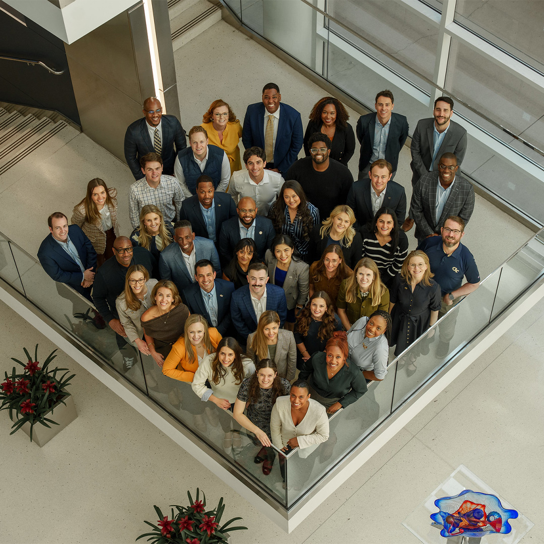 A group of women and men dressed in suit jackets pose in the Scheller College of Business Atrium