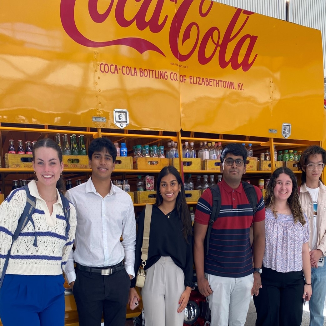 Students pose in front of an original 1949 yellow delivery truck found in the rotunda of Coke's Central Reception Building.