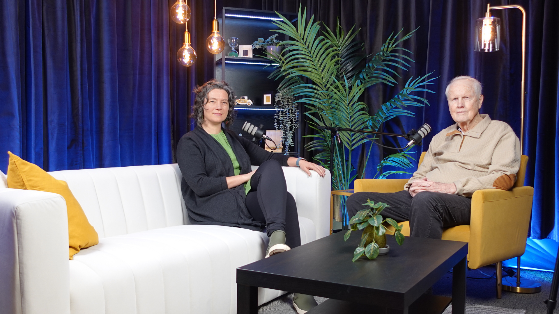 A man and a woman sitting down to record a podcast episode.
