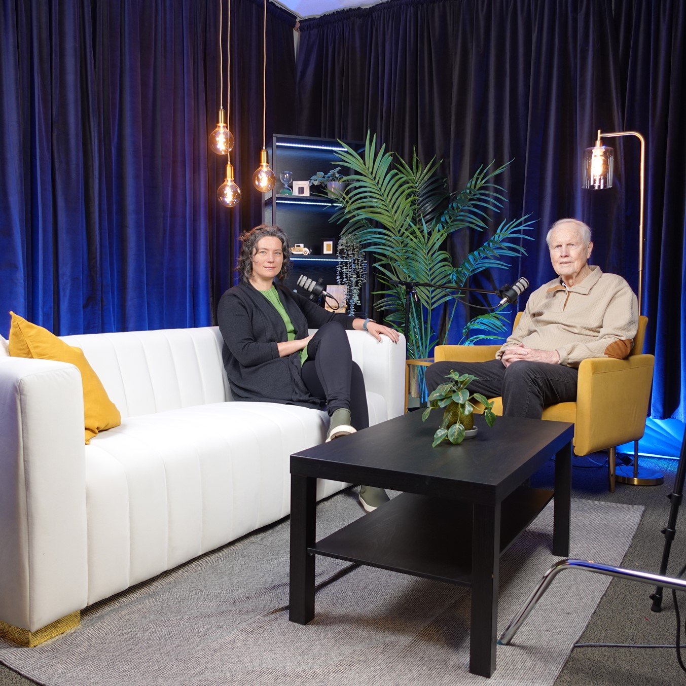 A man and a woman sitting down to record a podcast episode.